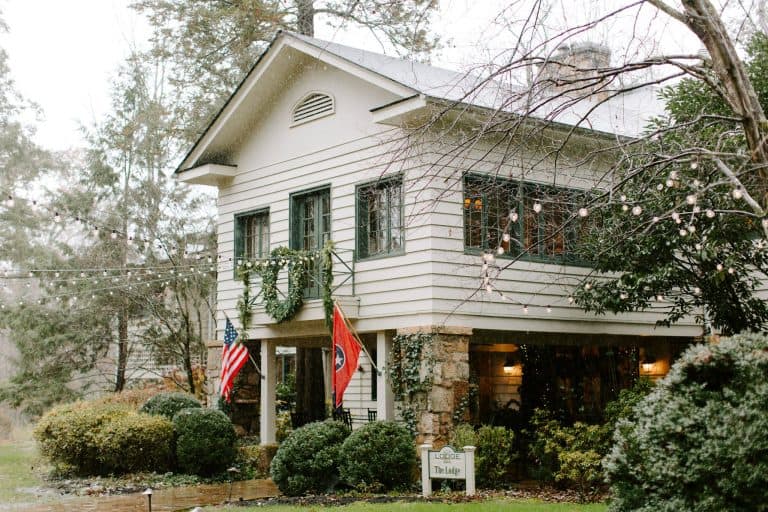 The white clapboard main house of RT Lodge in Maryville, Tennessee, with green shutters, string lights, a garland and American and Tennessee flags on the porch.