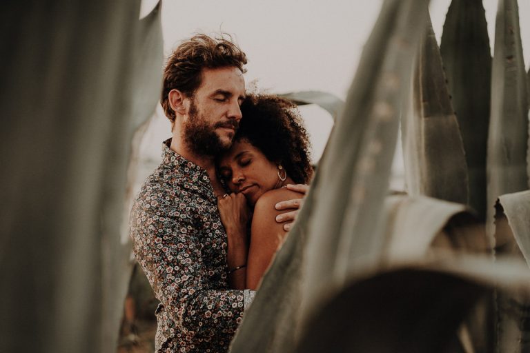 A bearded man holds a woman close, her head resting on his chest, in warm evening light in Sicily