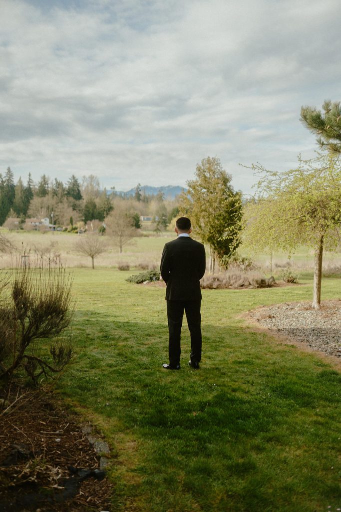 groom standing on a lawn waiting for his bride