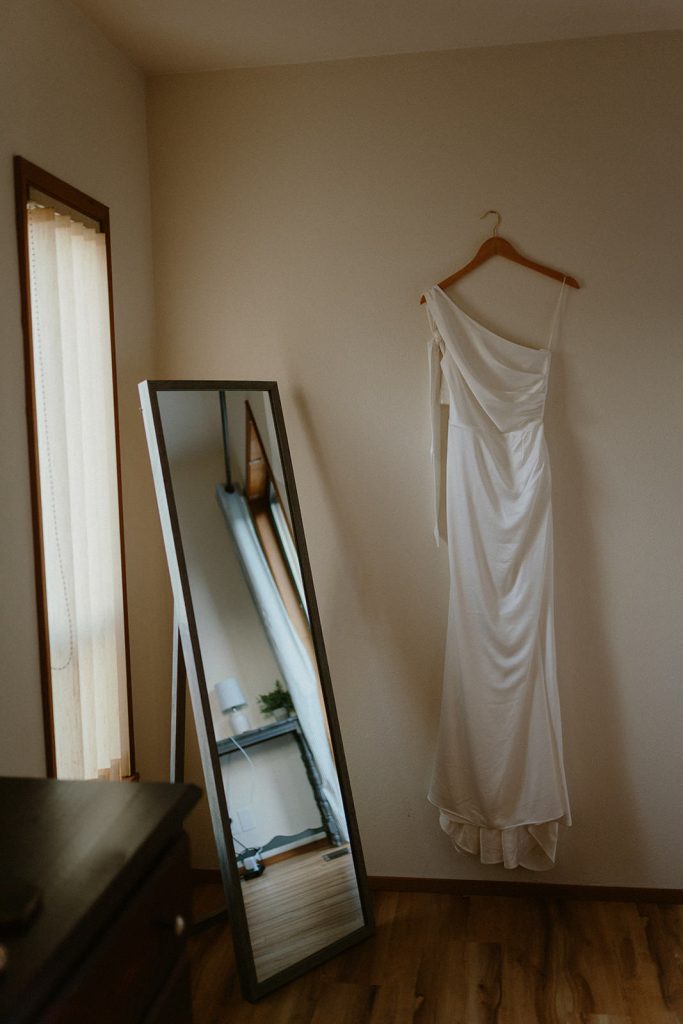 A bridal dress hanging next to a mirror