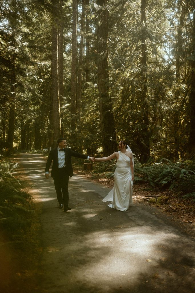 a groom and a bride walking through a lush forest